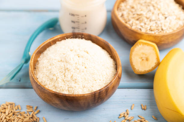 Powdered milk and oatmeal, banana baby food mix, infant formula, pacifier, bottle, spoon on blue wooden background. Side view, selective focus, artificial feeding concept.